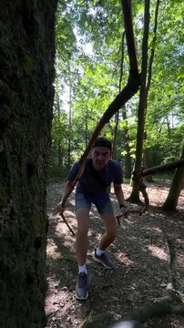 adult man grasping two twisted vine branches and lunging forward through shaded deciduous forest, knees bent and weight shifted as he navigates vegetation, focused
