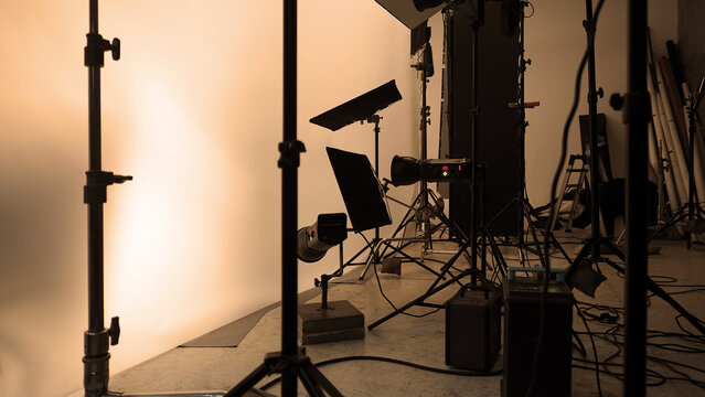 Shooting studio for photographer and creative art director with production setting up lighting flash and LED headlight on tripod and professional equipment for portrait model or product photo shoot.