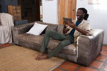Man smiling and holding tablet while sitting on leather sofa in living room, barefoot, copy space © WavebreakMediaMicro