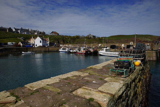 Fishing boats moored in St Abbs Harbour with stacks of lobster creels on the stone pier, Berwickshire, Scotland