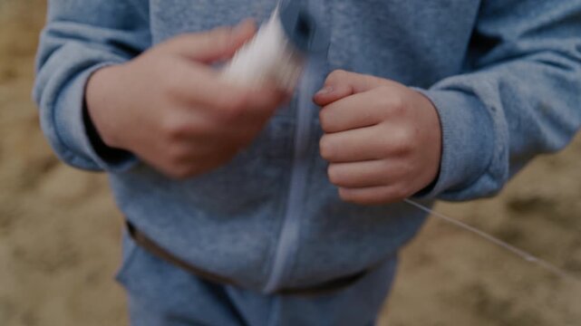 Young boy's hands quickly unwinding the string from a spool to fly a kite outdoors