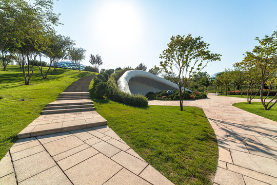 Beautiful modern public park with paved stone walkways, green lawns, and manicured topiary trees. Contemporary landscape design and urban architecture on a sunny summer day without people.