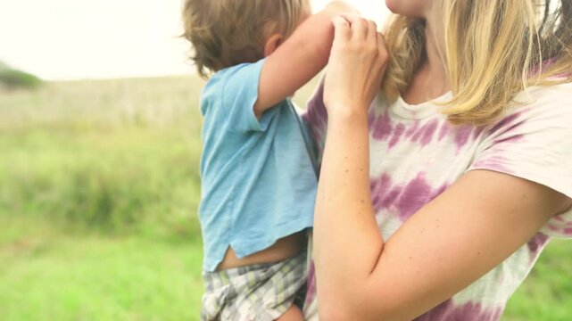 Toddler playfully grabbing his mother's arm during a close-up moment in a summer field