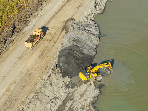 Aerial view of a heavy excavator digging gravel from water beside a dump truck during infrastructure construction at Autostrada A7 road junction in Bacau. Moldova Highway in Romania