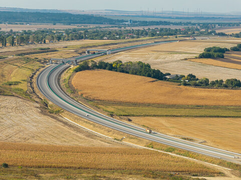 Aerial view of the Autostrada A7 highway construction near Bacau, featuring winding asphalt roads cutting through golden agricultural fields in bright daylight. Moldova Highway in Romania