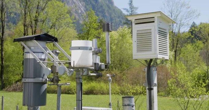 Handheld medium shot with slight camera breathing showing detailed meteorological instruments at a weather station, including a Stevenson screen and various sensors.