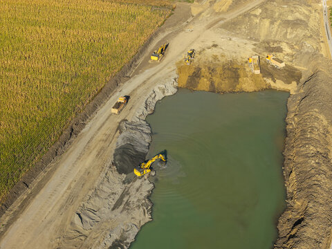 Aerial view of heavy excavators and dump trucks working near a pond on the Autostrada A7 motorway junction construction site in Bacau under bright sunlight.