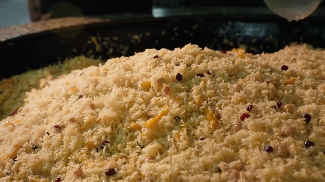 Traditional Uzbek wedding plov cooking in large kazan, oshpaz chef stirs steaming rice with a metal kapkir. Authentic Central Asian cuisine. Travel, tourism, gastronomy, cultural documentaries