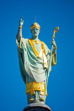 A bronze statue of Saint Martin holding a crosier stands against a clear blue sky.