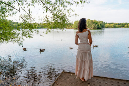 Woman standing by lake observing ducks in a natural setting during daylight Concept of relaxation, freedom, happiness, wellness and connection with nature