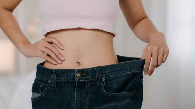 Weight loss success concept. Close-up of a slim waist with oversized jeans, representing healthy dieting, body transformation and fitness progress. Weight loss, waist, diet, fitness, health.