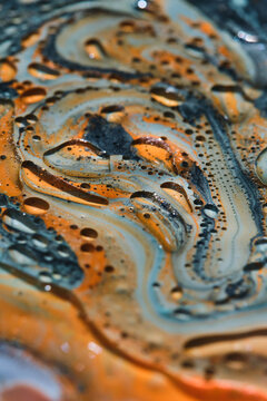 Vertical macro shot of swirling orange, light blue, and black paint with clear oil cell bubbles.