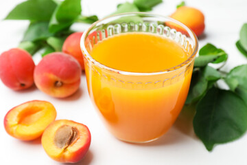Glass of apricot juice, fresh apricots and leaves on white table, closeup © New Africa