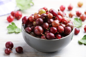 Fresh red gooseberries in bowl and green leaves on wooden table, closeup © New Africa