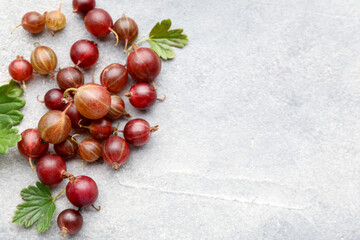 Fresh red gooseberries and green leaves on grey table, flat lay. Space for text © New Africa