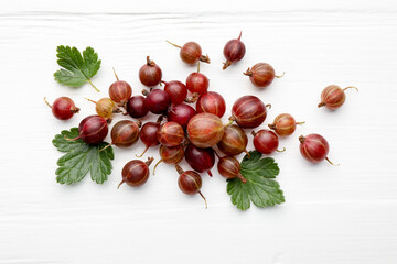 Fresh red gooseberries and green leaves on white wooden table, flat lay © New Africa