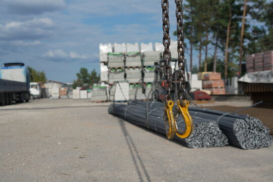 Heavy lifting hooks and chains in the foreground above bundled steel rebar at an industrial construction materials warehouse, highlighting metal handling and heavy-duty equipment.