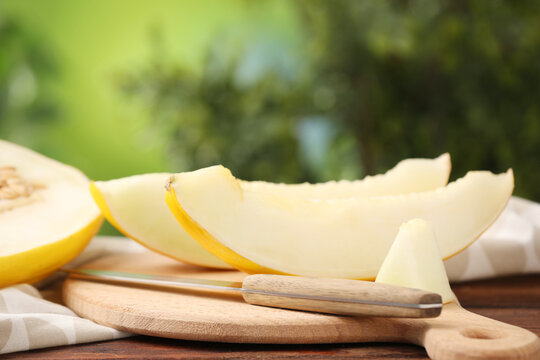 Slices of fresh sweet melon and knife on wooden table outdoors, closeup