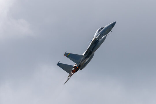 Side view of a F-15 Eagle climbing  with afterburners on, against clouds