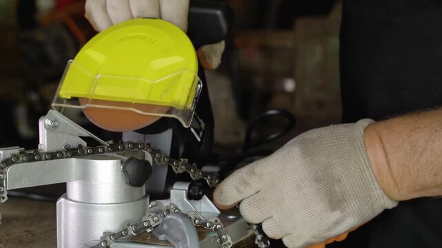Worker in gloves operates a chain sharpener with a yellow guard, sparks flying as the chain is adjusted, showcasing the detailed process of sharpening in a workshop setting