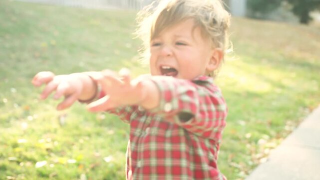 Toddler in a red plaid shirt laughing excitedly while walking on a leaf-covered sidewalk