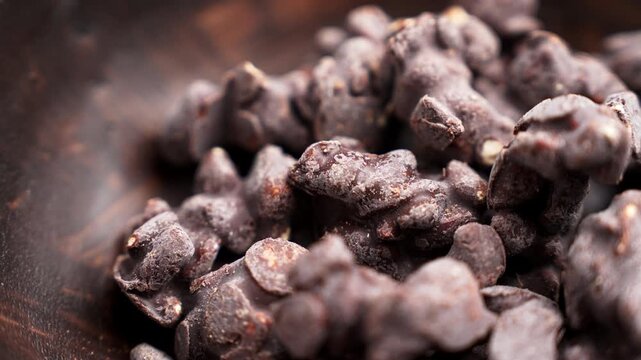Close-up view of assorted nuts coated in dark chocolate piled on a rustic wooden surface. Rotation