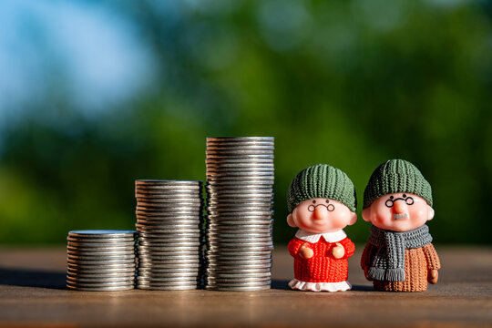 Cute elderly couple figurines standing next to three rising stacks of silver coins on wooden surface with green background. Perfect for retirement, pension planning, and savings concepts