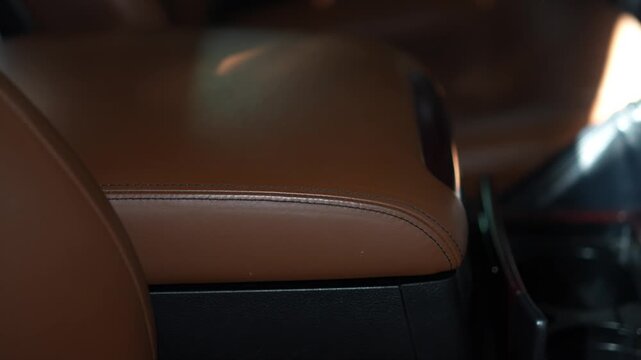 Car center console armrest upholstered in brown leather with black stitching.