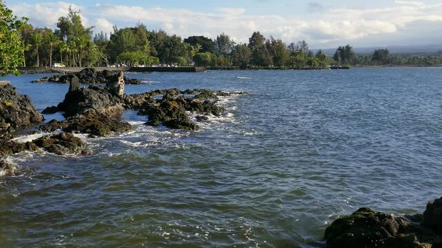 View from Coconut Island (Moku Ola) in Hilo Bay, Hilo, Hawaii. Located on the east side of the big island. Shot on a hazy late afternoon on a spring day April, 2023. Volcanic rocky shores and park.