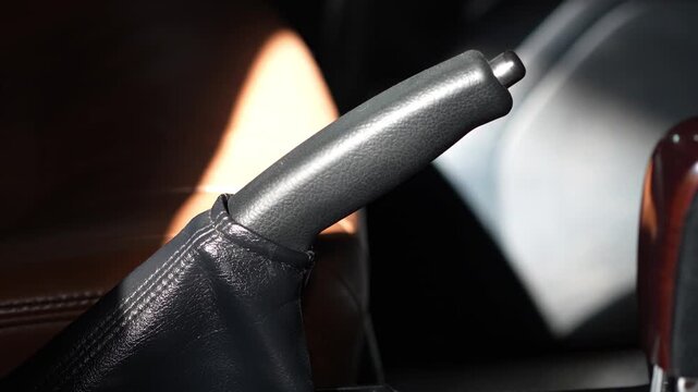 Car mechanical handbrake lever with a black textured plastic handle, a silver release button, and a black leather protective boot.
