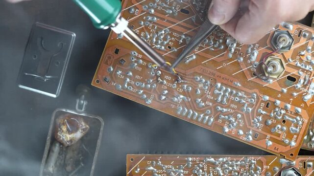 Close-up of technician's hand soldering components on a vintage electronic circuit board with a green soldering iron. Ideal for repair services, engineering, and DIY electronics concepts