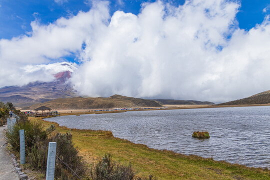 A beautiful panoramic view of the lake Limpiopungo and the majestic, snow-capped Cotopaxi active volcano partially covered by clouds in Cotopaxi National Park, Ecuador