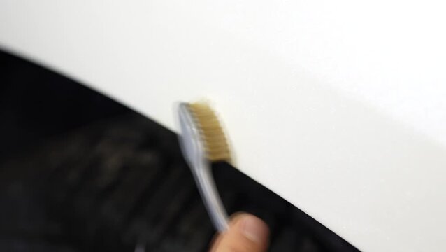 Detailer using a brush to clean dirt from the car fender gap.