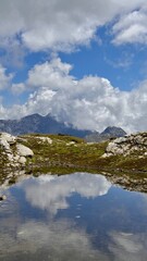 Fototapeta premium Mountains reflected in a calm pond during daytime with clouds and blue sky