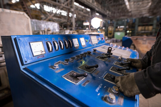 Factory worker operating blue industrial control panel with gauges and levers in warehouse setting