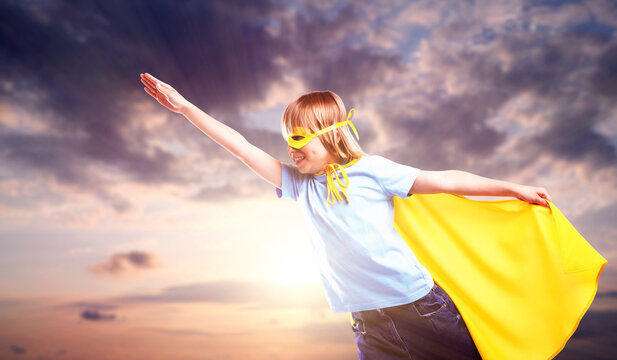 Little boy with yellow superhero cape and mask against sunset sky