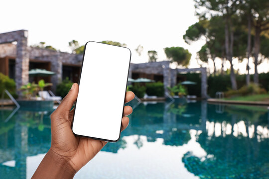 Man holding mobile phone with blank screen on sea resort by swimming pool, closeup
