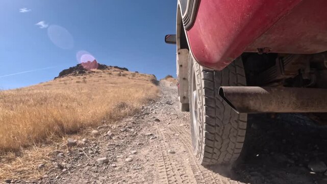 Low-angle view of red 4x4 ascending steep, rocky dirt trail