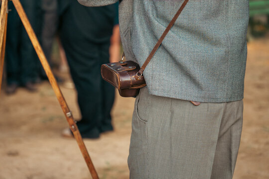 A side view shows a person in retro grey clothing carrying a vintage camera inside a brown leather case with a shoulder strap.