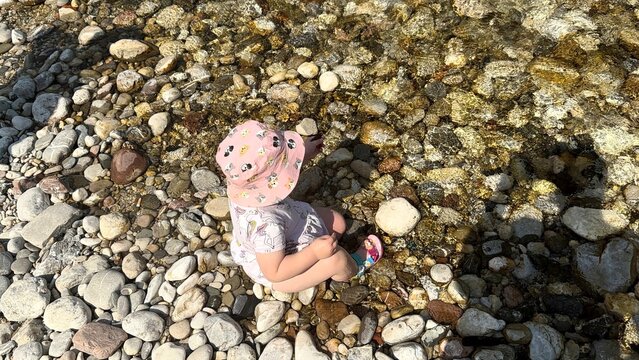 Little Child Exploring Stones by a Clear River in Nature on a Sunny Summer Day