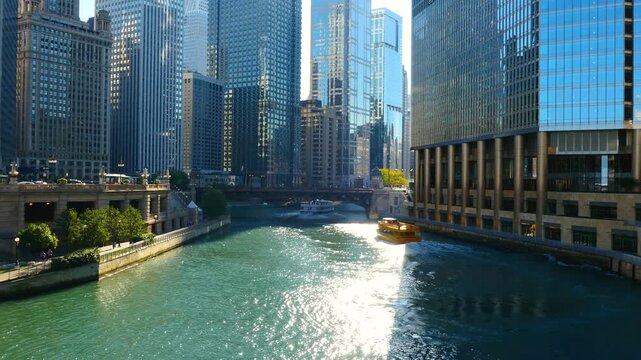 Scenic view of the Chicago River flowing through downtown, featuring iconic skyscrapers, historic bridges, and tour boats navigating the urban waterway on a sunny day.