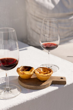 Portugese egg tart served on a wooden cutting board with glass of port wine on a patio with afternoon shadows