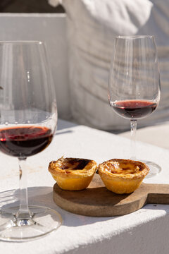 Portugese egg tart served on a wooden cutting board with glass of port wine on a patio with afternoon shadows