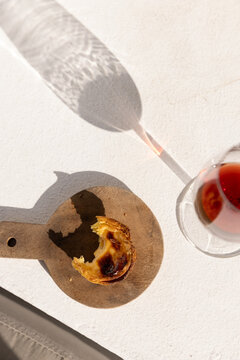 Portugese egg tart served on a wooden cutting board with glass of port wine on a patio with afternoon shadows