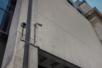 Wide view of surveillance cameras and cable trunking on a stone and concrete facade in central London under a classical cornice. © Victor