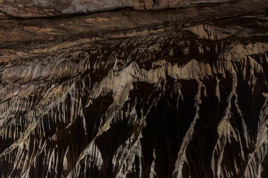 Rippling flowstone formations inside a limestone show cave at Cheddar Gorge, warm brown draperies lit from below.