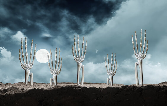 Skeleton hands emerging from dark dirt reaching up toward a spooky night sky with full moon