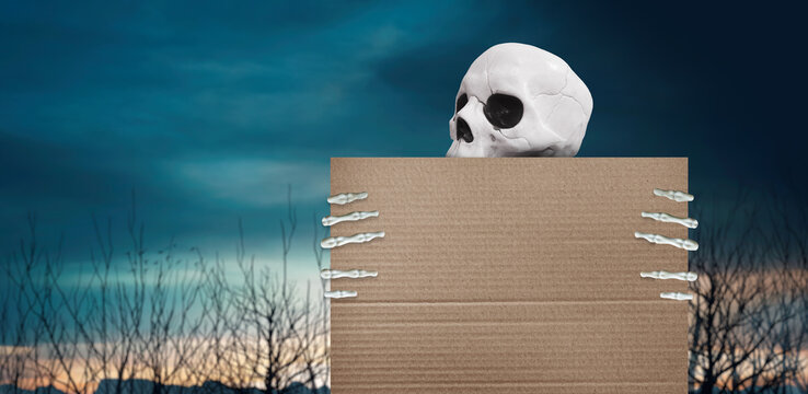 White skull and skeleton hands holding a blank cardboard sign against a spooky twilight landscape with bare trees