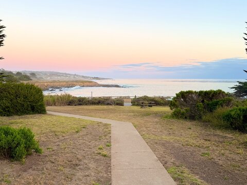 Paved path leading towards the scenic Pacific Ocean coastline at sunset in Cambria, California