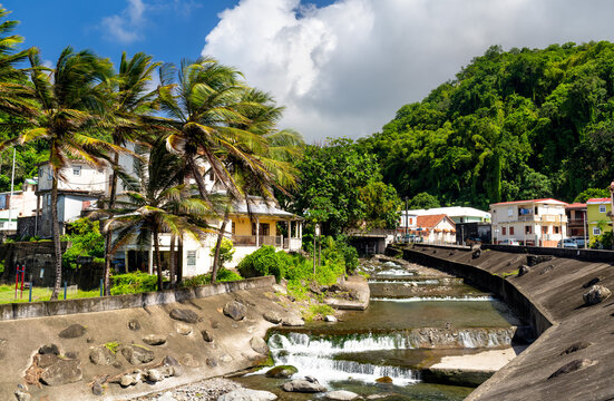 A beautiful view of the Grand Riviere river with small waterfalls flowing through the tropical town of Grand Riviere in Martinique, surrounded by palm trees and lush hills